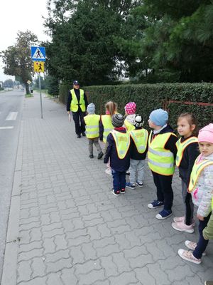 Dzieci w kamizelkach odblaskowych idą w stroną przejścia dla pieszych.